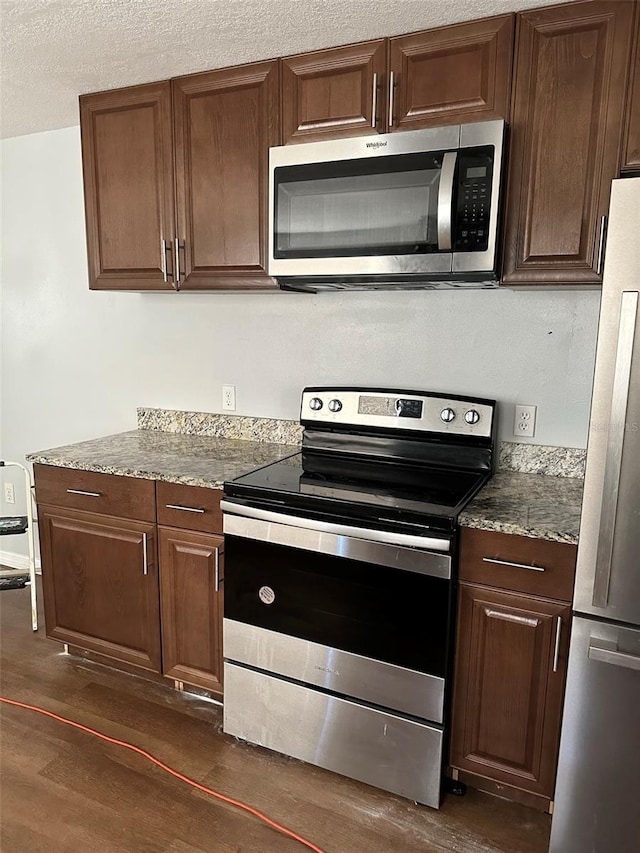 kitchen with light stone countertops, stainless steel appliances, and dark hardwood / wood-style floors