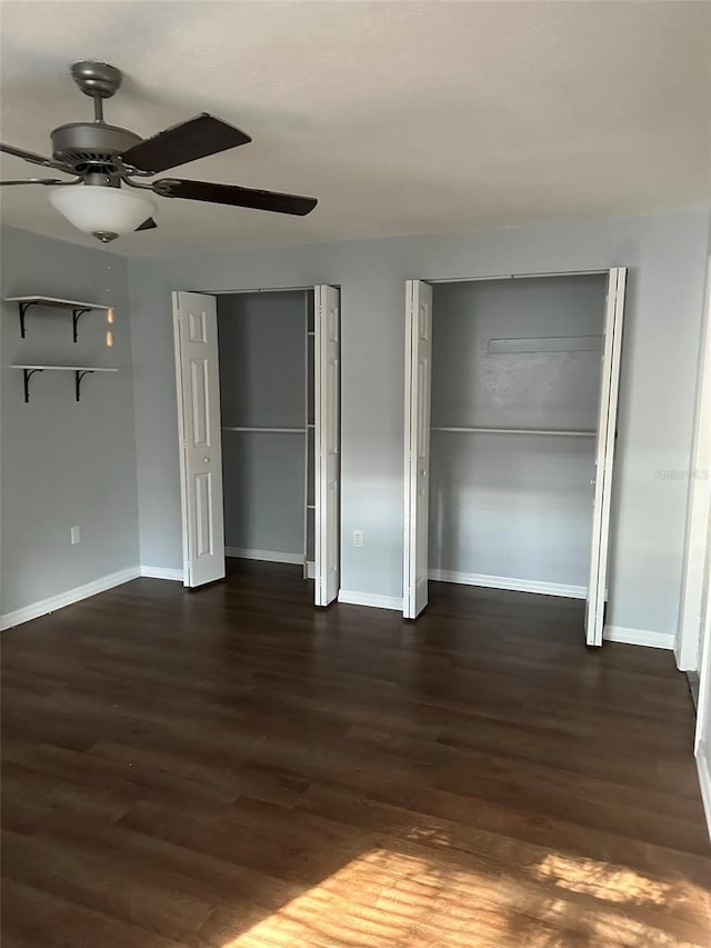 unfurnished bedroom with two closets, ceiling fan, and dark wood-type flooring