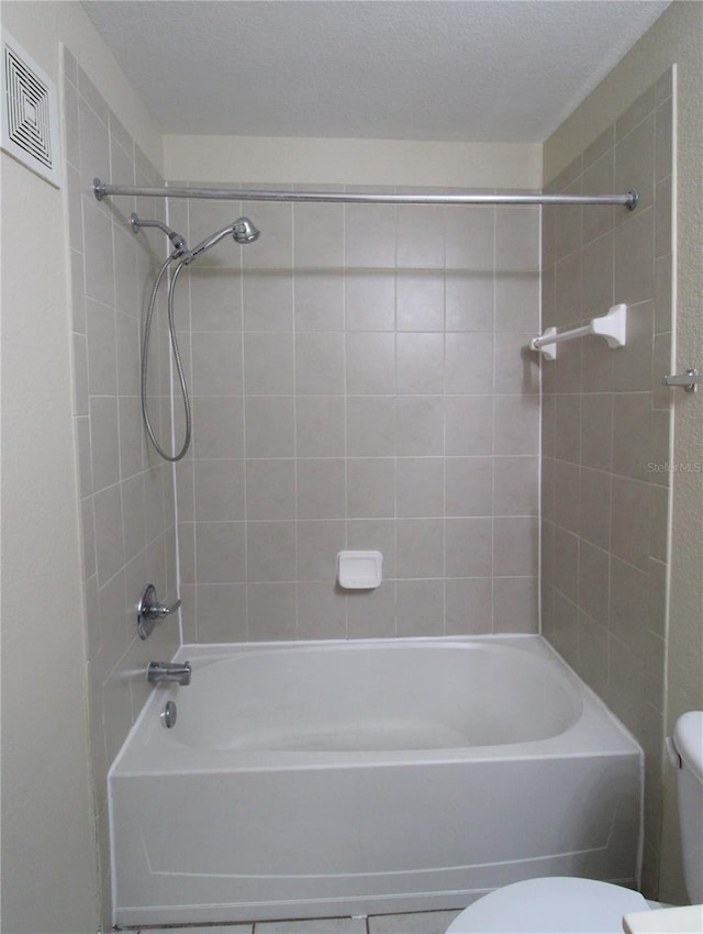 bathroom with tiled shower / bath, a textured ceiling, and toilet