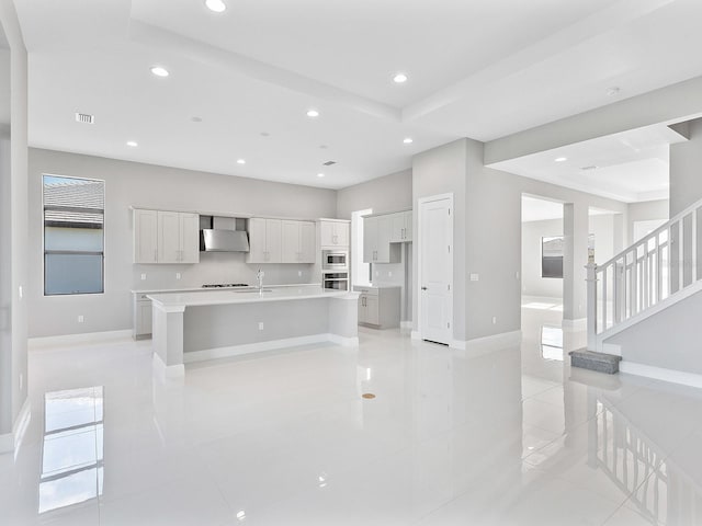 kitchen featuring white cabinets, a spacious island, wall chimney exhaust hood, appliances with stainless steel finishes, and light tile patterned flooring