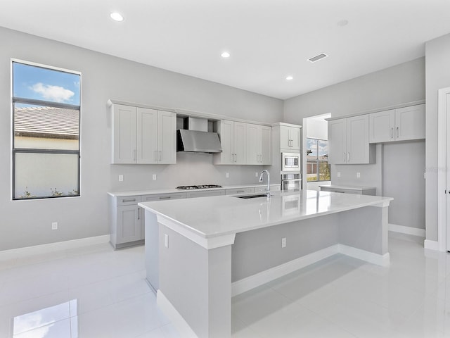 kitchen featuring a wealth of natural light, stainless steel appliances, a kitchen island with sink, sink, and wall chimney range hood