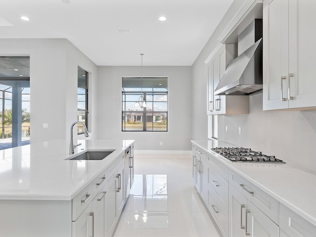 kitchen featuring white cabinetry, sink, wall chimney exhaust hood, light stone counters, and decorative light fixtures