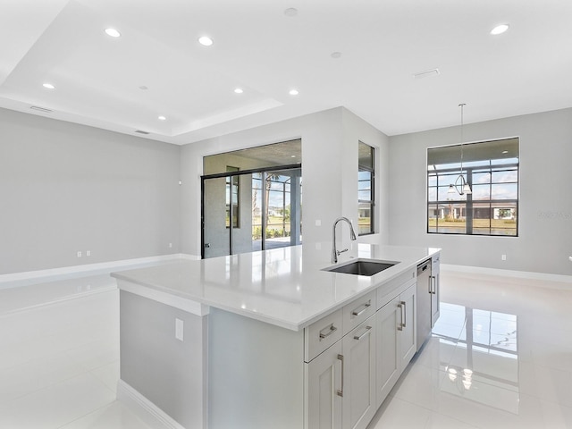 kitchen featuring a tray ceiling, a kitchen island with sink, a healthy amount of sunlight, and sink