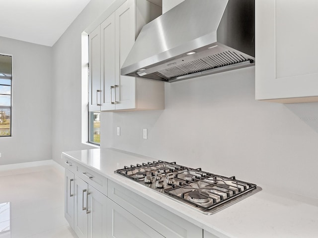 kitchen featuring plenty of natural light, white cabinets, wall chimney range hood, and stainless steel gas cooktop