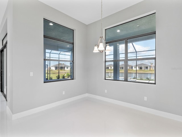 spare room with tile patterned flooring, a water view, an inviting chandelier, and plenty of natural light