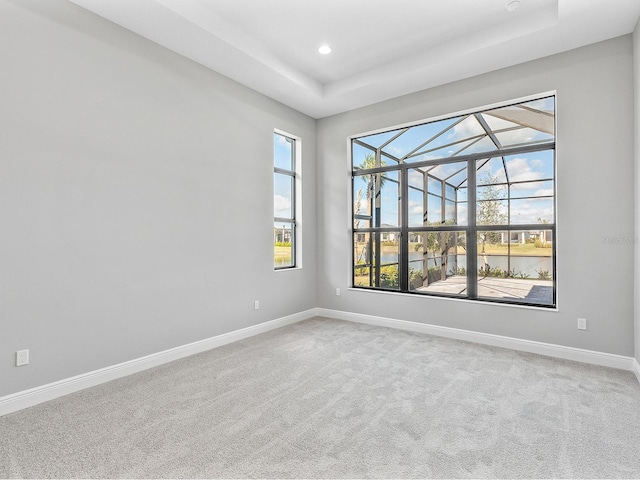 unfurnished room with a water view, carpet floors, and a tray ceiling