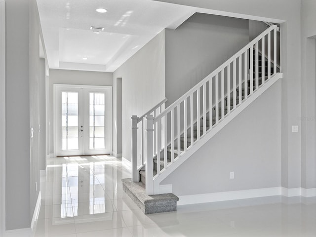 entryway featuring a raised ceiling, french doors, and light tile patterned flooring