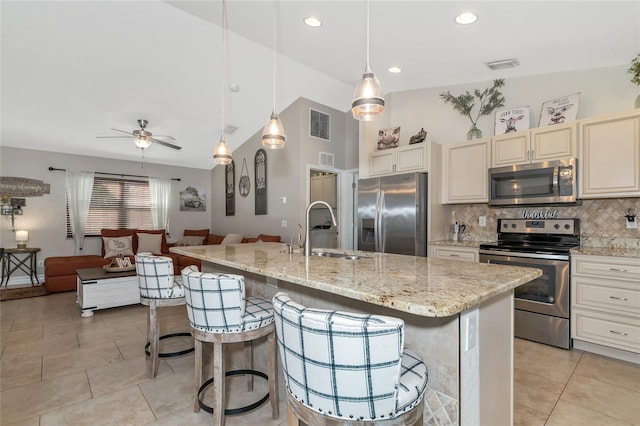 kitchen featuring a kitchen bar, stainless steel appliances, a kitchen island with sink, sink, and decorative light fixtures