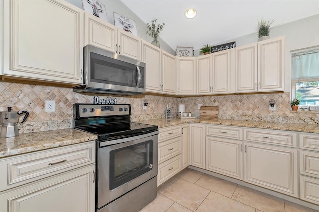 kitchen with light stone countertops, appliances with stainless steel finishes, light tile patterned floors, cream cabinetry, and lofted ceiling