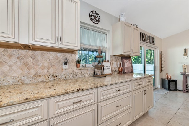 kitchen with tasteful backsplash, light stone countertops, light tile patterned floors, and lofted ceiling