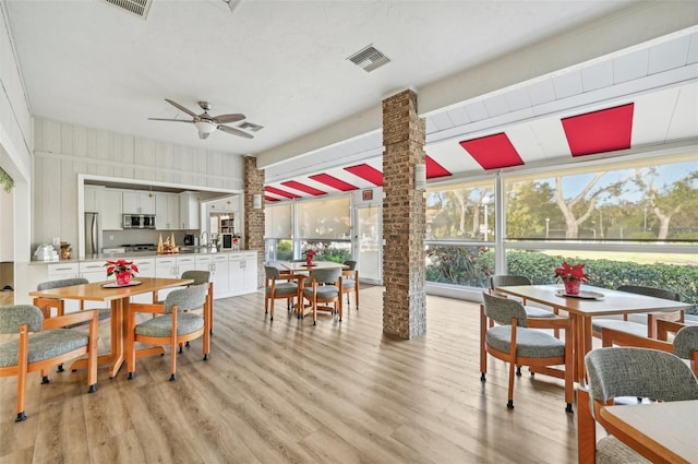 dining area with decorative columns, ceiling fan, and light wood-type flooring