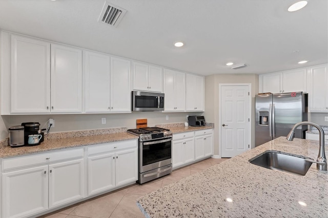 kitchen with light stone countertops, stainless steel appliances, sink, light tile patterned floors, and white cabinets