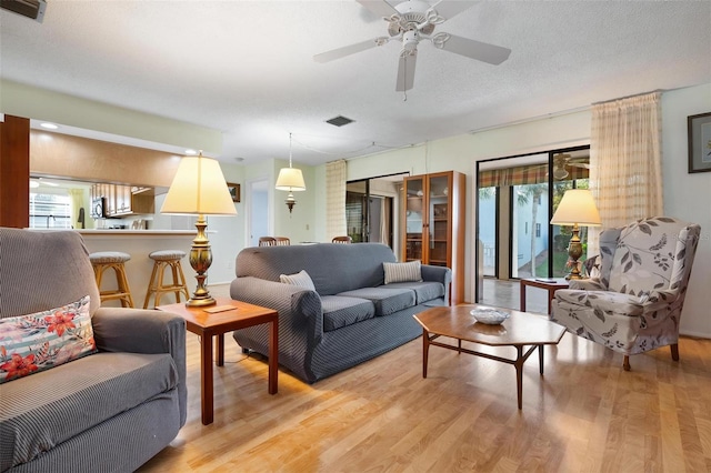 living room featuring ceiling fan, light hardwood / wood-style floors, and a textured ceiling