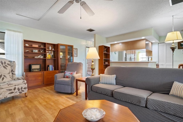 living room with ceiling fan, light wood-type flooring, and a textured ceiling