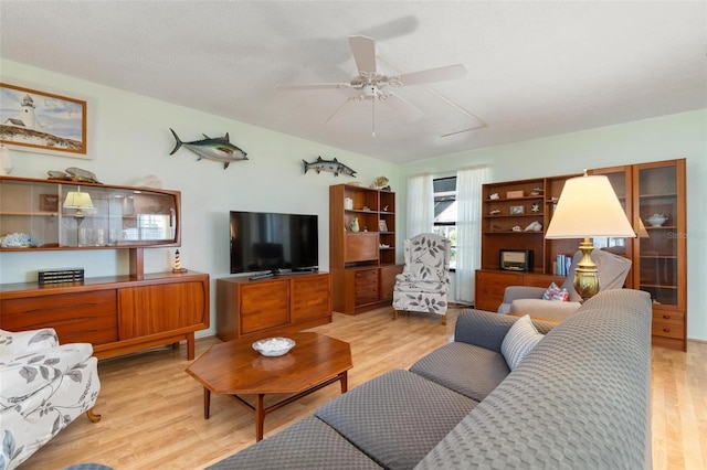 living room with ceiling fan, light wood-type flooring, and a textured ceiling