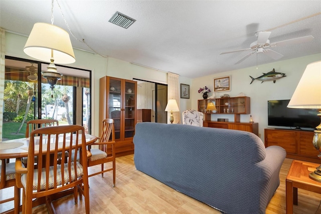 living room with ceiling fan, light wood-type flooring, and a textured ceiling