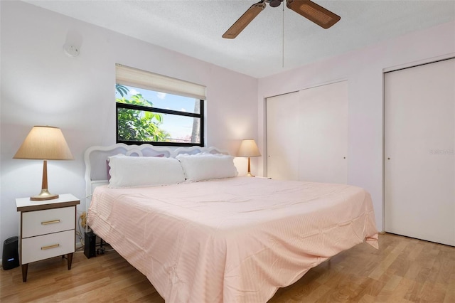 bedroom featuring a textured ceiling, ceiling fan, light hardwood / wood-style flooring, and two closets