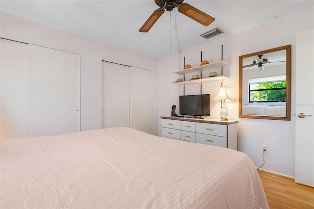 bedroom featuring light wood-type flooring, ceiling fan, and multiple closets