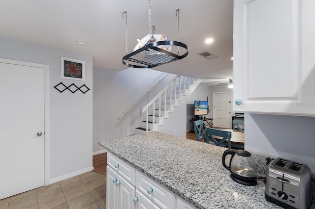 kitchen with light tile patterned floors, white cabinetry, ceiling fan, and light stone counters