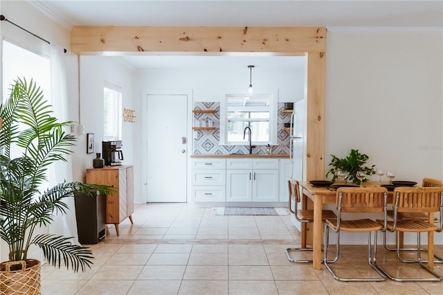 interior space with sink, hanging light fixtures, white cabinets, crown molding, and light tile patterned flooring