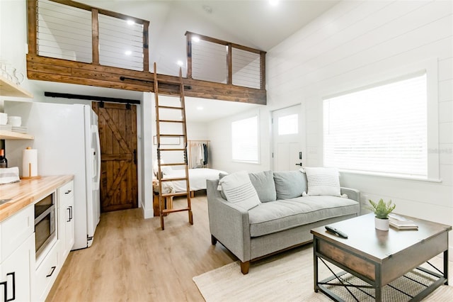 living room with a barn door, light hardwood / wood-style floors, high vaulted ceiling, and a wealth of natural light