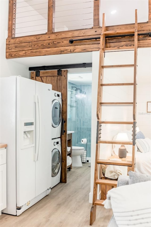 clothes washing area with light hardwood / wood-style floors and stacked washer / drying machine