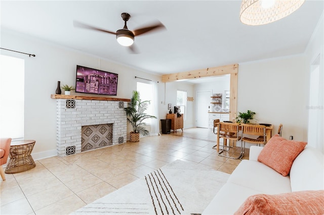 living room with light tile patterned floors, a brick fireplace, ceiling fan, and crown molding