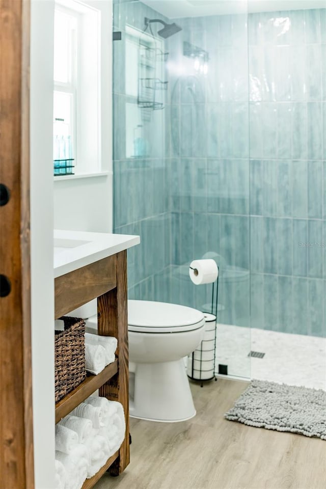 bathroom featuring a tile shower, wood-type flooring, toilet, vanity, and tile walls