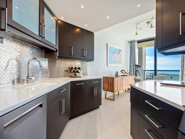 kitchen featuring tasteful backsplash, light stone counters, dishwashing machine, dark brown cabinets, and sink