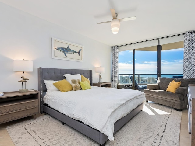 bedroom with access to exterior, ceiling fan, a water view, and a wall of windows