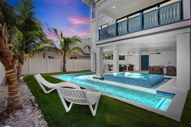 pool at dusk with an in ground hot tub, ceiling fan, a patio, and an outdoor hangout area