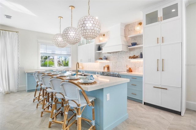 kitchen with pendant lighting, a breakfast bar, white cabinets, an island with sink, and custom range hood