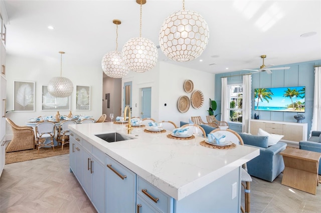 kitchen with light stone countertops, sink, ceiling fan, hanging light fixtures, and a kitchen island with sink