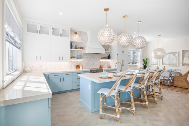 kitchen featuring decorative light fixtures, custom exhaust hood, a wealth of natural light, and an island with sink