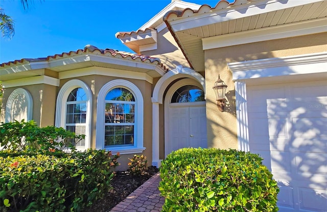 doorway to property with a garage, a tiled roof, and stucco siding