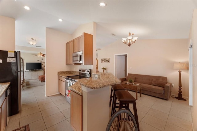 kitchen featuring kitchen peninsula, a kitchen bar, light stone counters, stainless steel appliances, and lofted ceiling