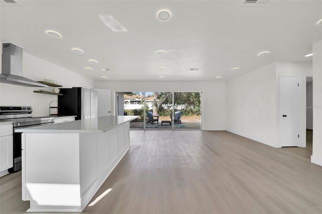 kitchen featuring black refrigerator, wall chimney range hood, stainless steel electric range oven, light wood-type flooring, and white cabinetry