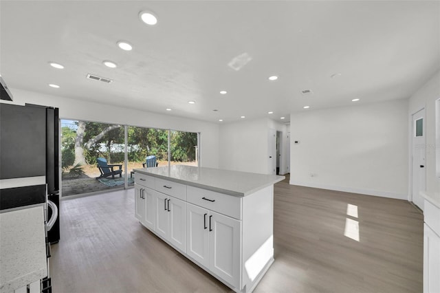 kitchen with white cabinets, a center island, light hardwood / wood-style floors, and light stone countertops