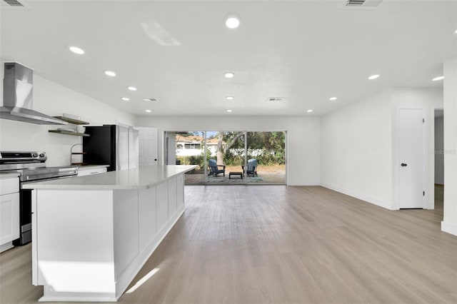 kitchen with wall chimney exhaust hood, black fridge, electric stove, white cabinets, and light wood-type flooring