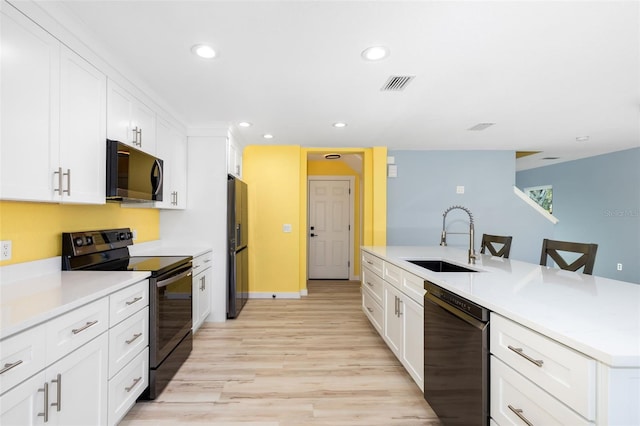 kitchen featuring sink, a breakfast bar, white cabinetry, black appliances, and light hardwood / wood-style floors