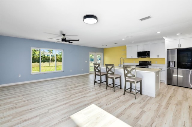 kitchen featuring a breakfast bar, white cabinets, stainless steel appliances, a center island with sink, and light wood-type flooring