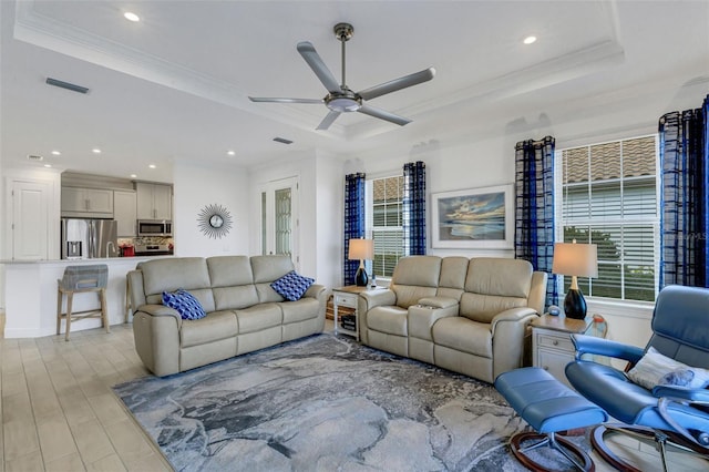 living room featuring a raised ceiling, crown molding, ceiling fan, and light wood-type flooring