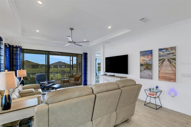 living room featuring a raised ceiling, ceiling fan, crown molding, and light wood-type flooring