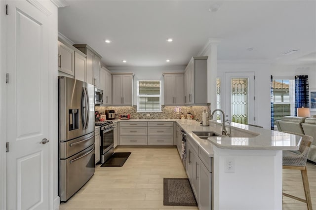 kitchen with appliances with stainless steel finishes, tasteful backsplash, ornamental molding, sink, and light hardwood / wood-style floors