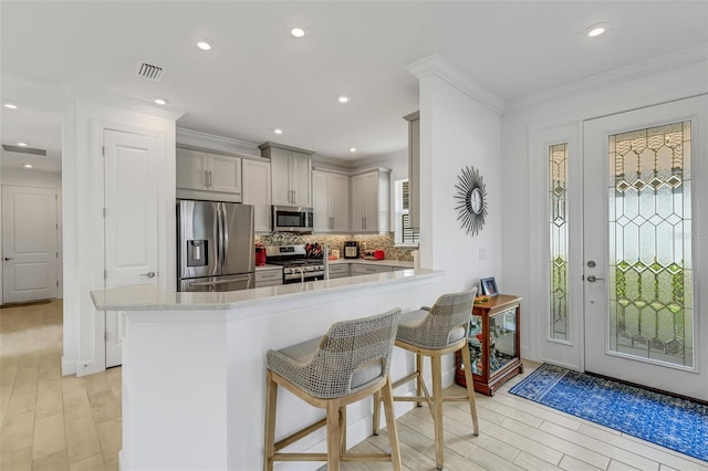 kitchen featuring stainless steel appliances, a kitchen breakfast bar, backsplash, kitchen peninsula, and light wood-type flooring