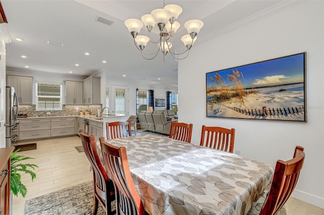 dining area featuring a healthy amount of sunlight, light wood-type flooring, crown molding, and an inviting chandelier