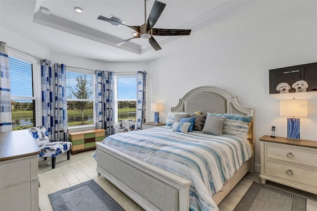 bedroom with a raised ceiling, ceiling fan, light wood-type flooring, and ornamental molding