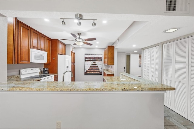 kitchen featuring white appliances, sink, ceiling fan, light stone counters, and kitchen peninsula