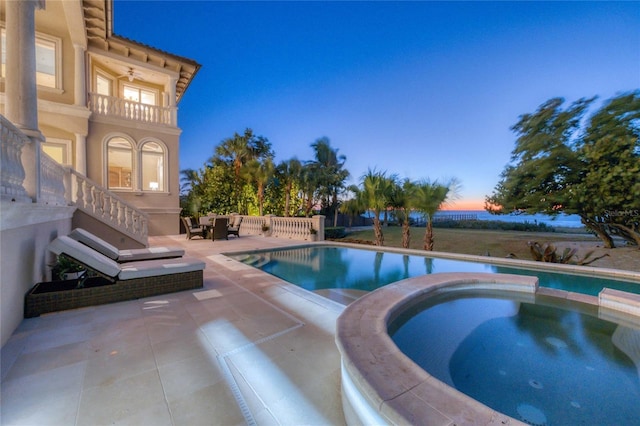 pool at dusk featuring a patio area and an in ground hot tub