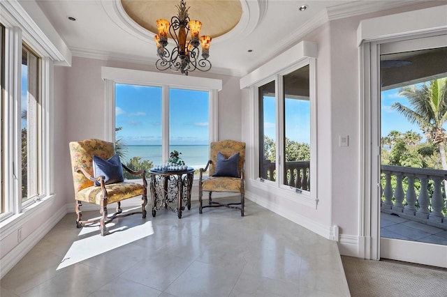 living area with a tray ceiling, a wealth of natural light, a water view, and a chandelier